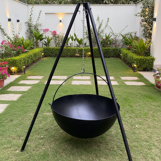 A large black outdoor fire pit standing on a tripod, placed on grass with shrubbery in the background.