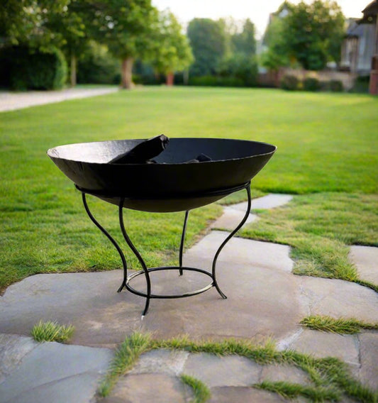 An outdoor wood and coal burning stove, known as a fire pit, placed on a stone surface with grass in the background.